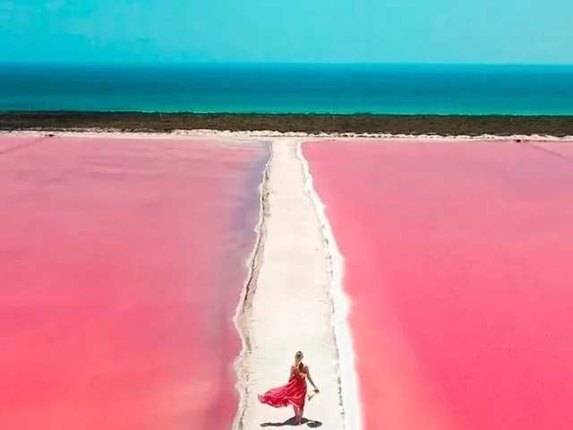 Une femme en robe rouge marchant sur un sentier à travers une lagune rose.