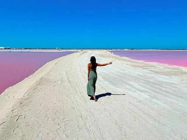 A woman walking on a white path between two sections of a pink lake.