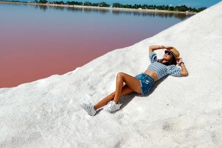 Eine Frau entspannt auf einem großen Haufen weißen Salzes neben einem rosa See.