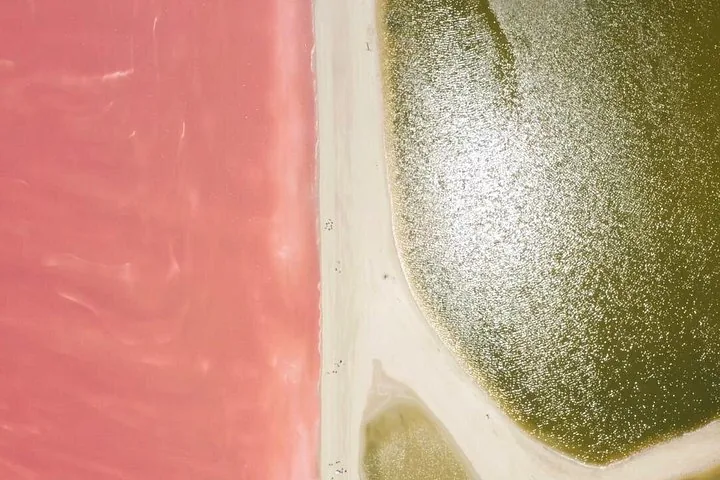 Aerial view showing a white path separating a pink lake from a green one.
