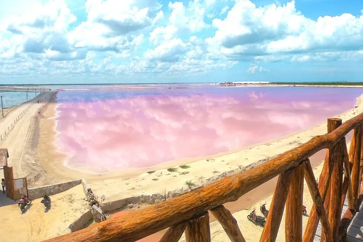 Een houten uitkijkplatform met uitzicht over een grote roze zoutlagune onder een bewolkte lucht.