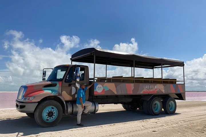 Ein Reiseleiter steht neben einem großen Ausflugstruck an einer rosa Lagune.