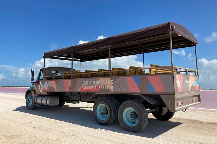 Ein leerer offener Ausflugstruck steht auf einem Sandweg nahe dem rosa Wasser.